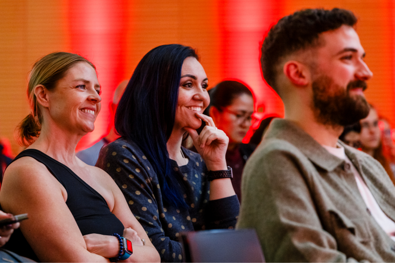 Fokus auf drei Personen im Publikum, die freudig an einer Veranstaltung teilnehmen,