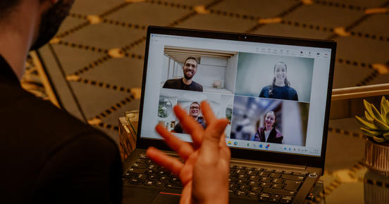 Person nimmt an einem Video-Call am Laptop teil; vier Teilnehmende sind im Raster auf dem Bildschirm zu sehen.