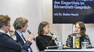Zwei Männer und zwei Frauen sitzen nebeneinander an einem Tisch. Der Mann und die Frau in der Mitte sprechen jeweils in ein Mikrofon. Die drei Personen links im Bild sind der Frau auf der rechten Seite zugewandt. Im Hintergrund zeigt ein Bildschirm den Titel der Veranstaltung "Autor:in und Verleger:in des Siegertitels im Börsenblatt-Gespräch" mit Dr. Stefan Hauck.