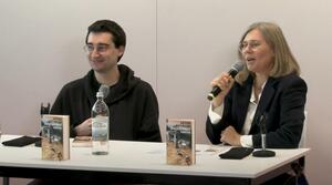 Ein Mann und eine Frau sitzen nebeneinander an einem Tisch. Die Frau auf der rechten Seite hält ein Mikrofon in ihrer rechten Hand, spricht und schaut zum Publikum. Der Mann auf der linken Seite schaut lächeln zum Publikum. Auf dem Tisch stehen zwei Exemplare eines Buches mit dem Titel "Angespannt vapen".