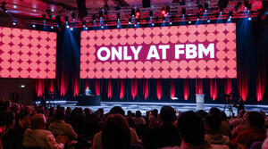 Ein großer Veranstaltungssaal mit Publikum und Bühne, auf einer Leinwand die Aufschrift "Only at FBM"
