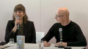 Eine Frau und ein Mann sitzen nebeneinander. Die Frau auf der linken Seite hält ein Mikrofon in ihrer rechten Hand und spricht zum Publikum. Der Mann auf der rechten Seite schaut sie an. Auf dem Tisch steht ein Buch mit dem Titel "Davon".