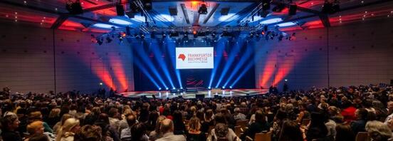 Blick auf eine Bühne in einem großen Saal mit Frankfurter Buchmesse Logo und viel Publikum.