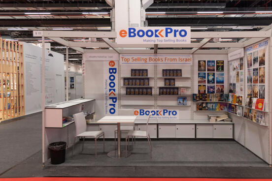 Foto von einem Messestand mit Tisch und Stühlen im Vordergrund und Bücherregalen im Hintergrund