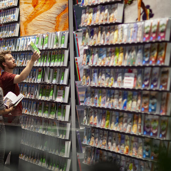 Drei Personen stehen vor einem Bücherdisplay. Ein Mann greift ein Buch aus dem Regal.